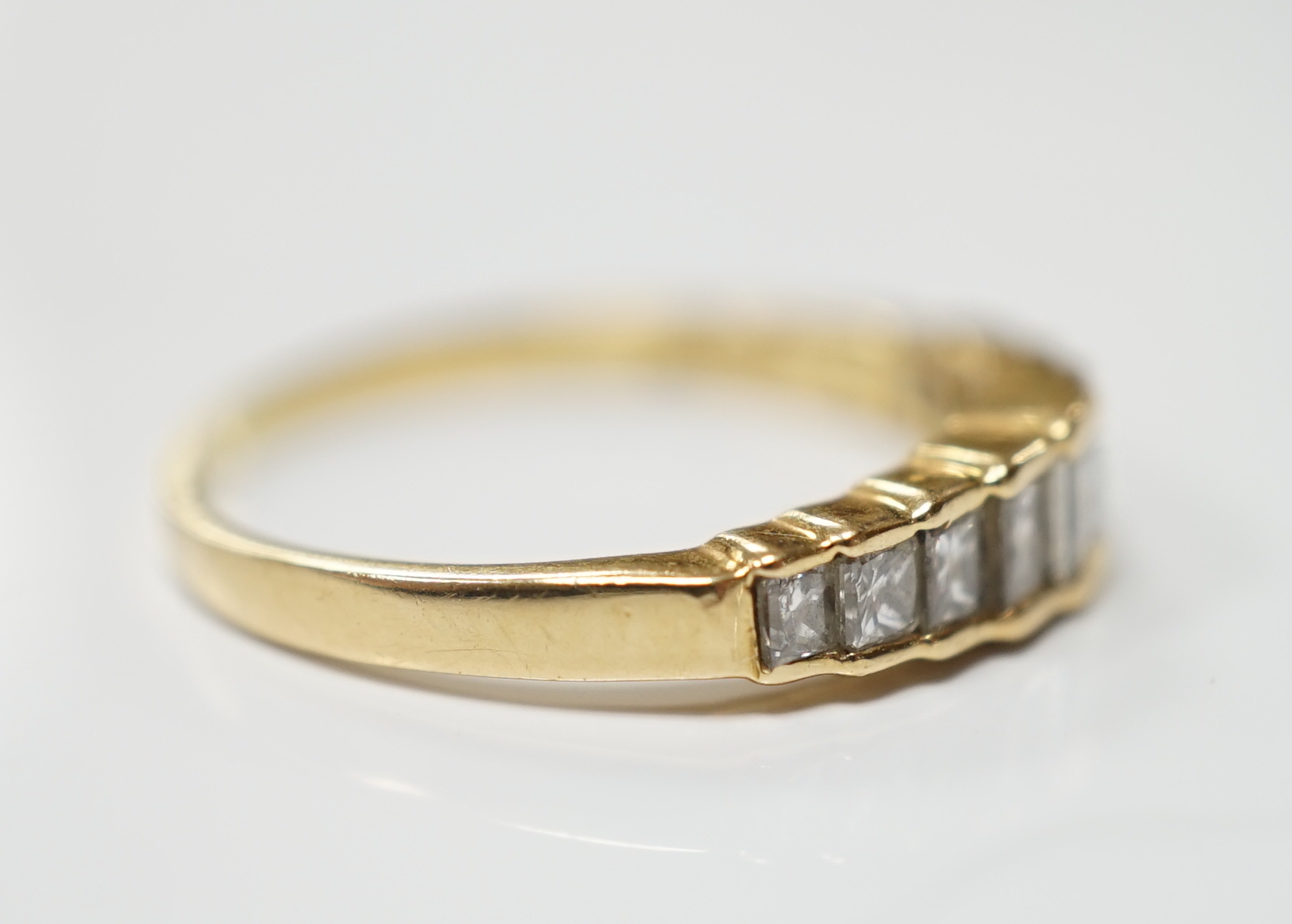 A modern 18ct gold and graduated nine stone princess cut diamond set half hoop ring, size L, gross weight 1.9 grams.